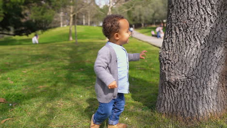 Little-boy-running-around-tree,-playing-hide-and-seek,-smiling